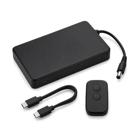 Slim matte black rechargeable battery box with a DC lead, a short USB-C cable and a small two-button remote, on white